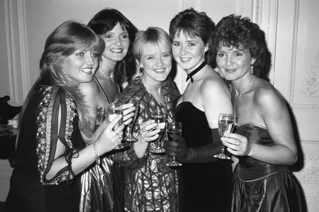 Five women in formal wear toasting with champagne flutes.