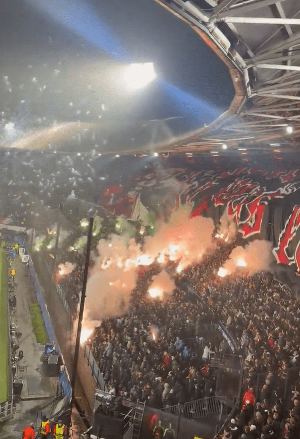 Stadium crowd igniting flares and smoke bombs.