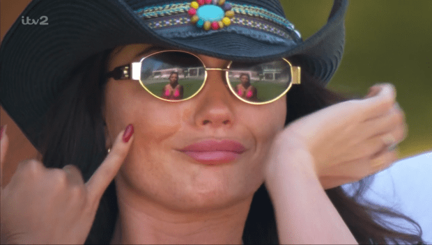 Woman wearing a cowboy hat and sunglasses; reflection in sunglasses shows two women in bikinis.