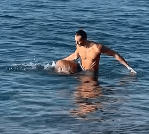 Man helping a dog swim in the ocean.