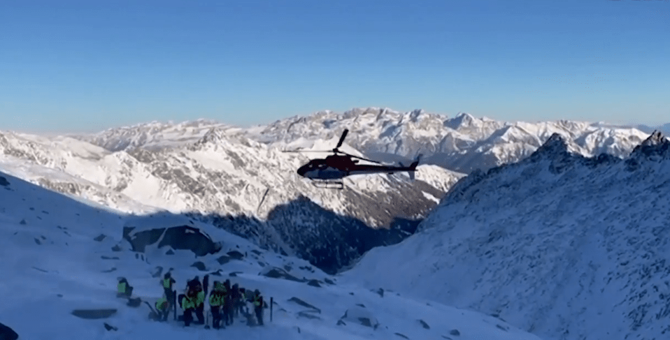 Helicopter over snowy mountains and rescue team.