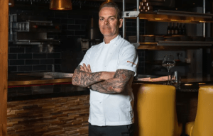 Portrait of a chef with tattoos, arms crossed.