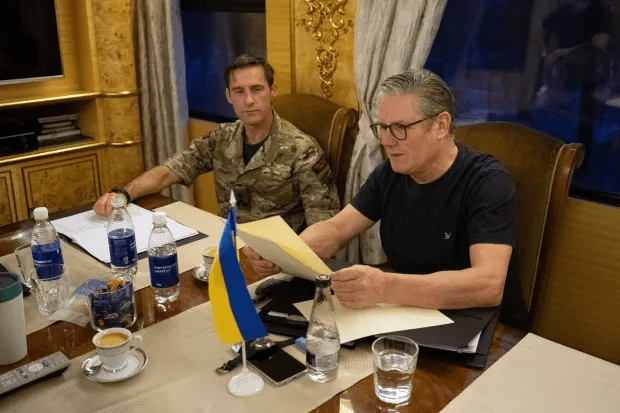 Two men reviewing documents at a table; a Ukrainian flag is visible.