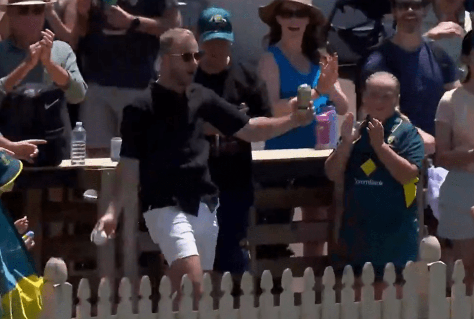 Man handing out items to cheering spectators behind a fence.