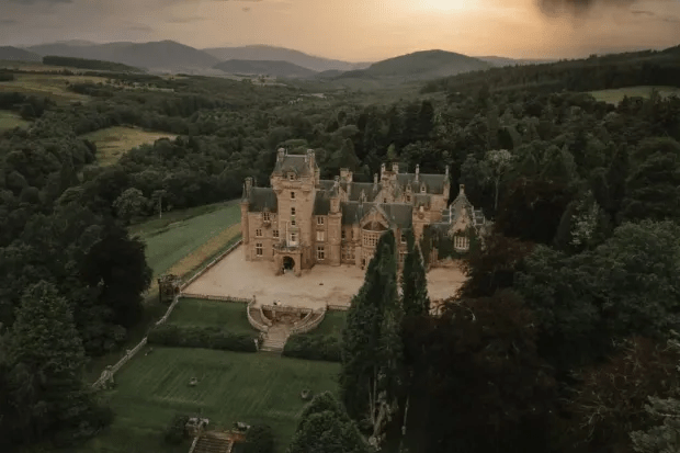 Aerial view of a large castle surrounded by trees and green landscape.