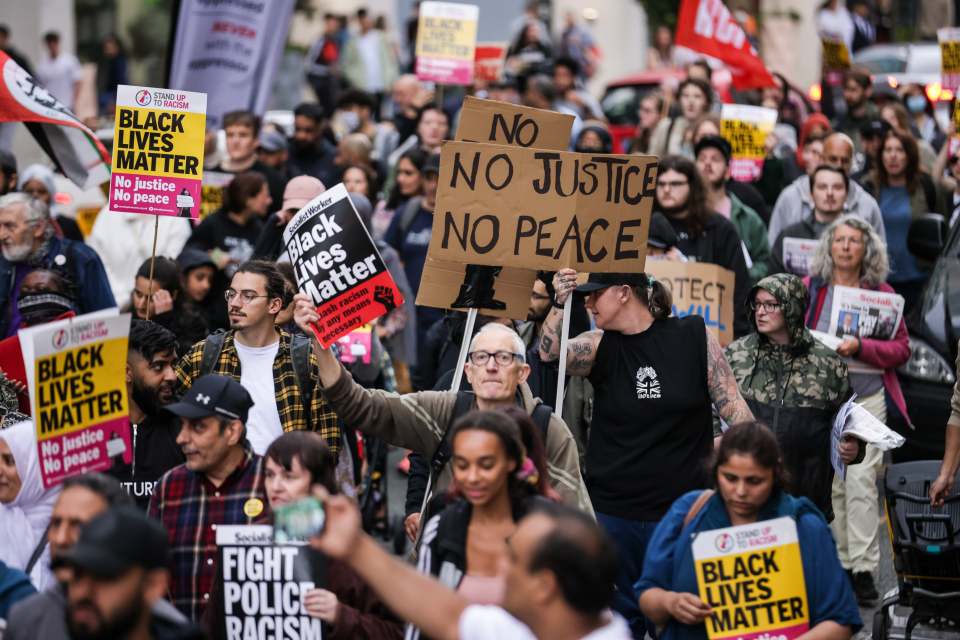 Protestors holding signs that read "Black Lives Matter" and "No Justice No Peace".