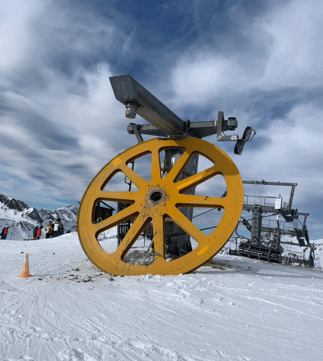 Large yellow ski lift pulley in snowy mountains.