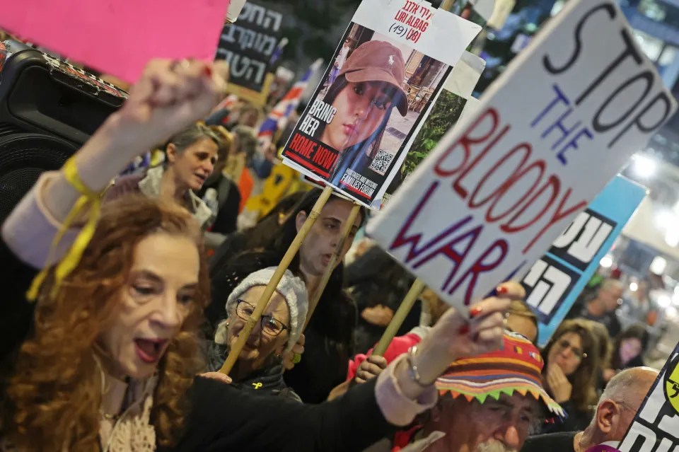 Protestors holding signs that read "Stop the Bloody War" and "Bring Her Home Now".