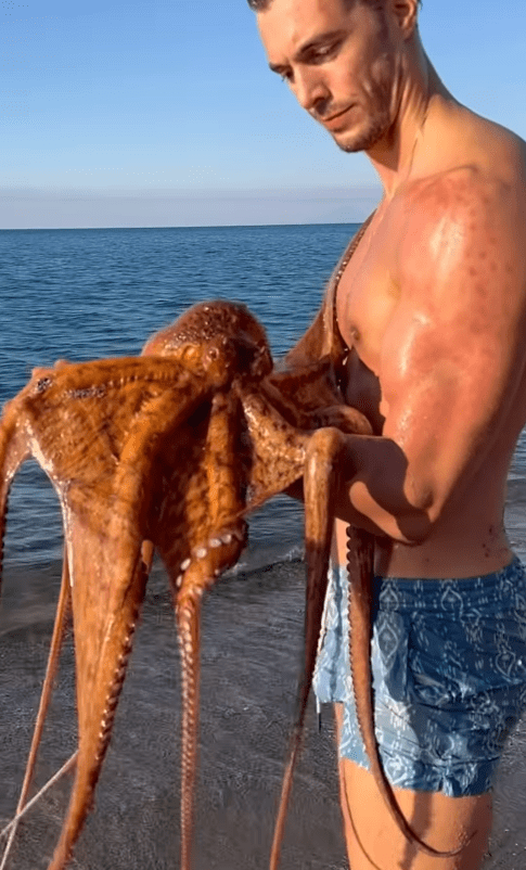 Man holding a large octopus on a beach.