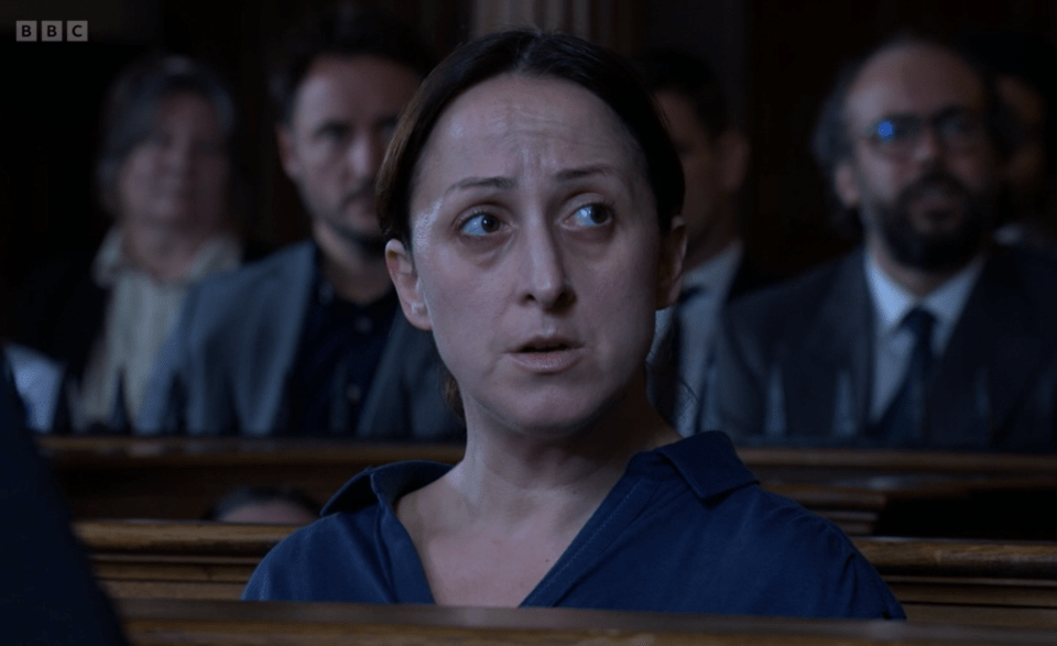 Woman in a dark blue shirt sitting in a courtroom.