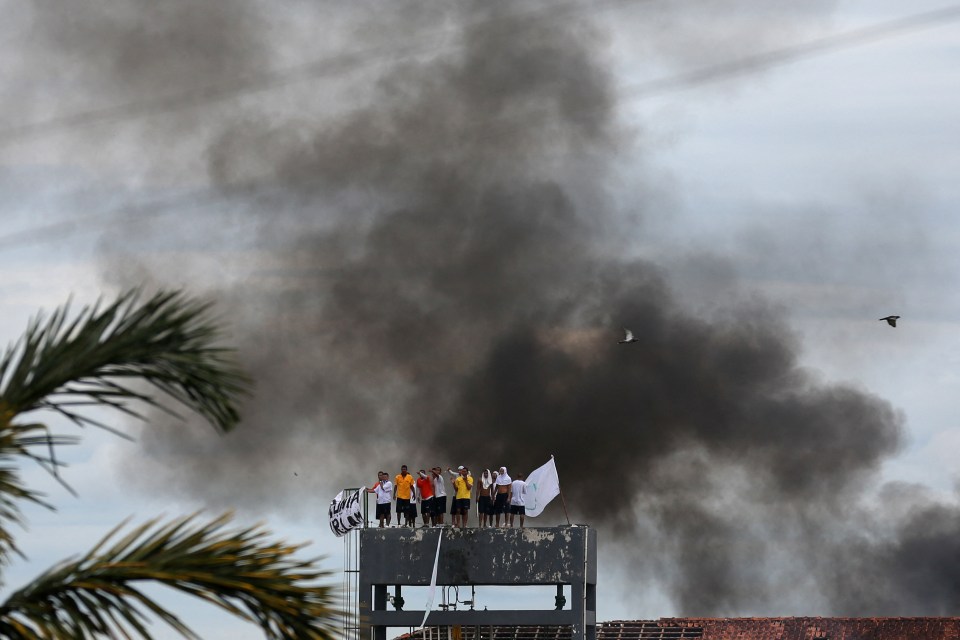 Inmates atop a prison tower during a rebellion, holding a banner and a white flag amidst smoke.