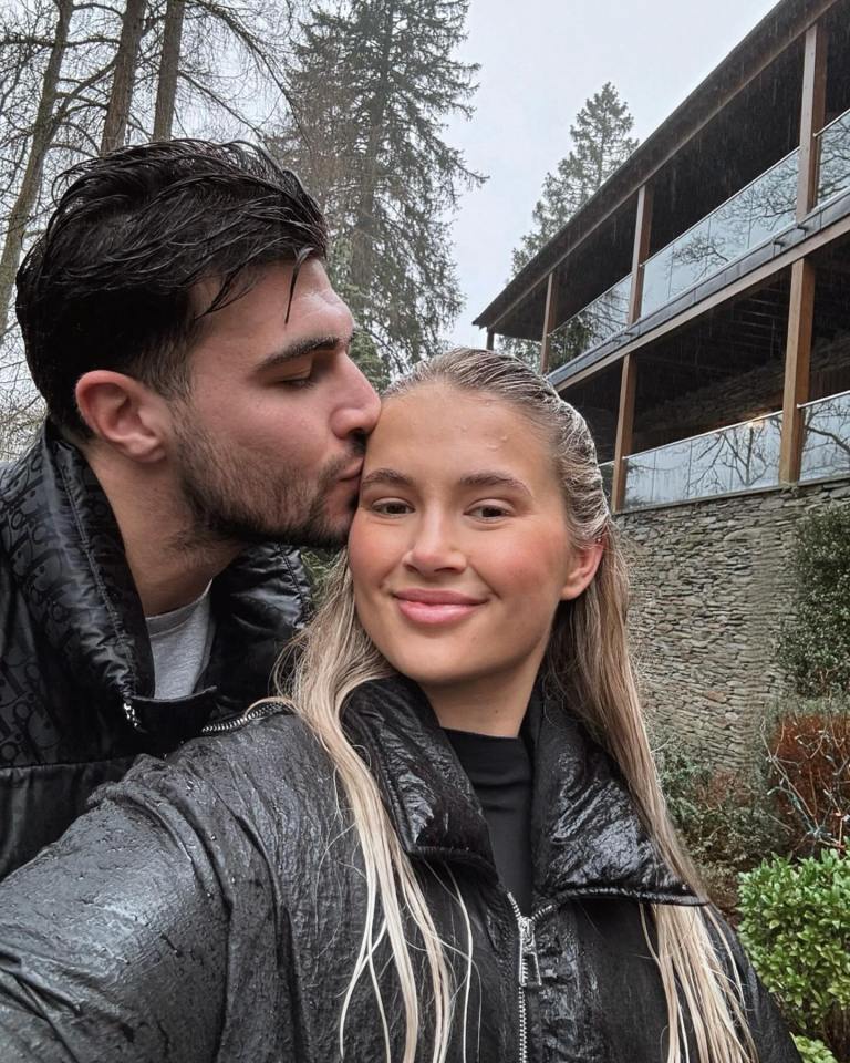 Couple kissing in the rain, near a stone building.