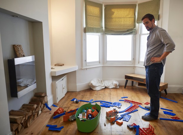 A man looking at scattered toys in a living room.