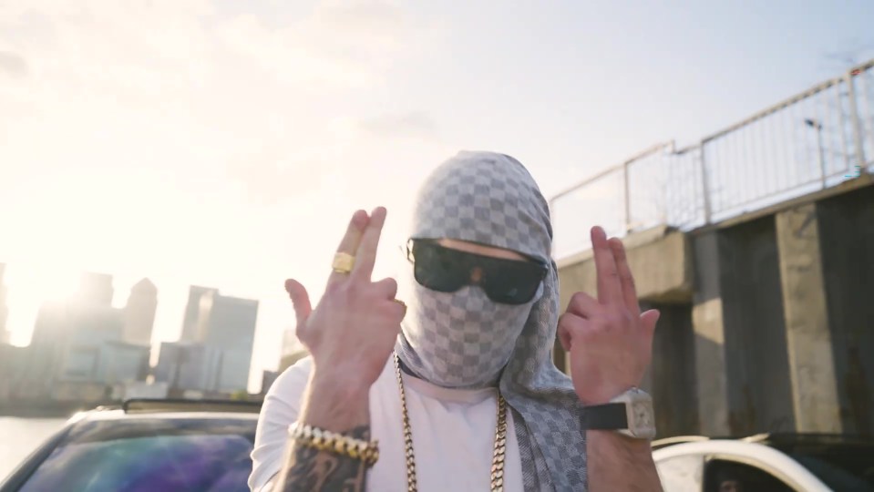 Screengrab of a man wearing a checkered balaclava and sunglasses making hand gestures.