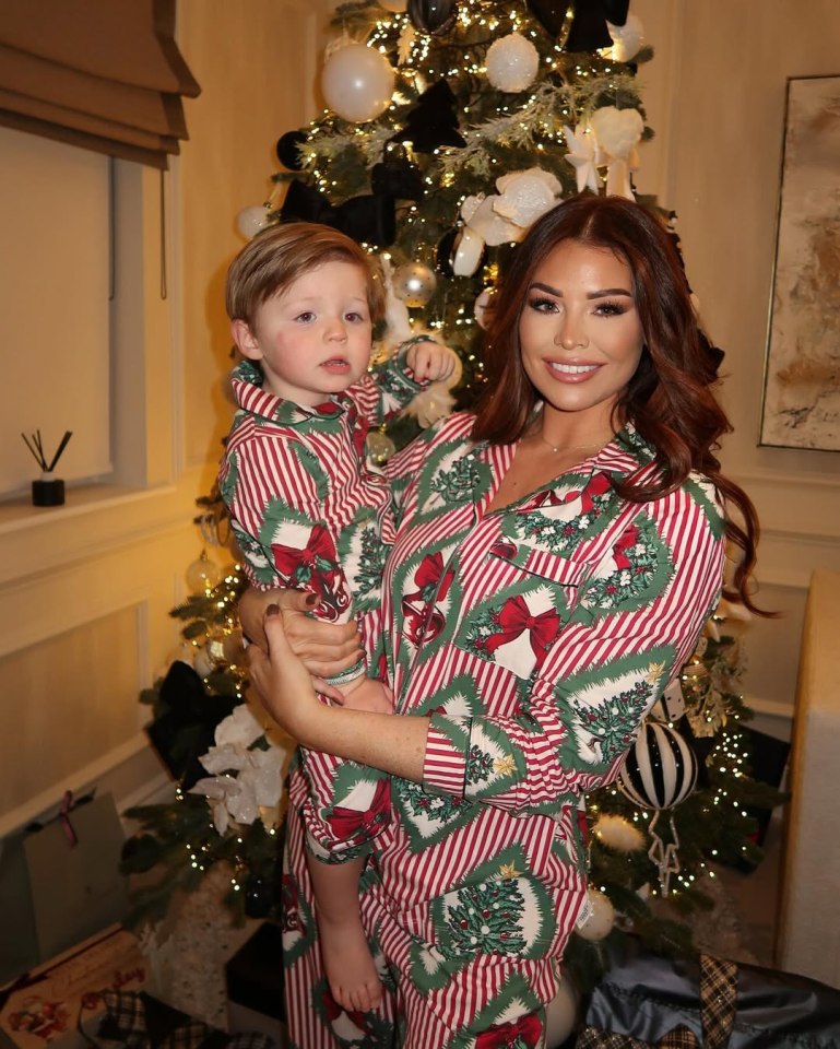 Woman and toddler in matching Christmas pajamas near a decorated tree.