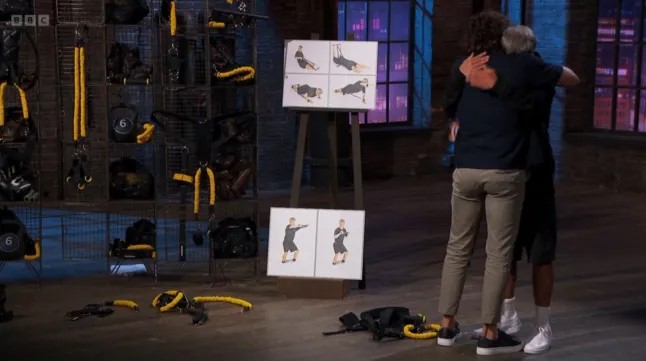 Joe Wicks on Dragon's Den, embracing an investor.  Workout equipment is visible.