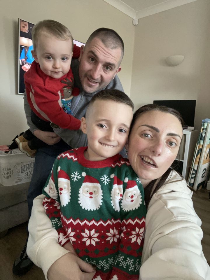 Family selfie; two parents and two young children in Christmas sweaters.