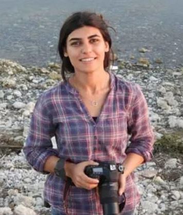 Woman holding a camera by a lake.