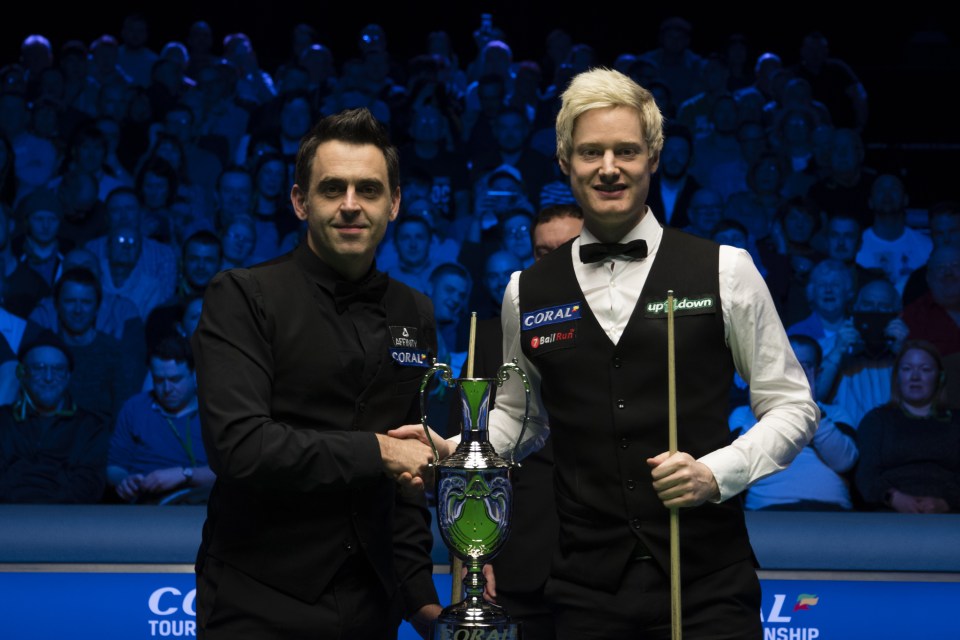 Ronnie O'Sullivan and Neil Robertson shake hands with a trophy.