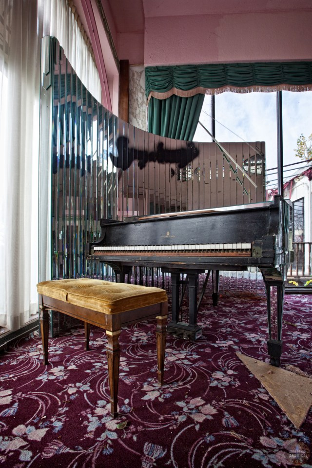 Piano and bench in abandoned hotel room.