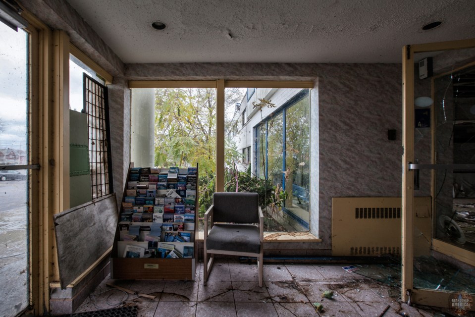 Interior of abandoned hotel lobby with a chair and brochure rack.