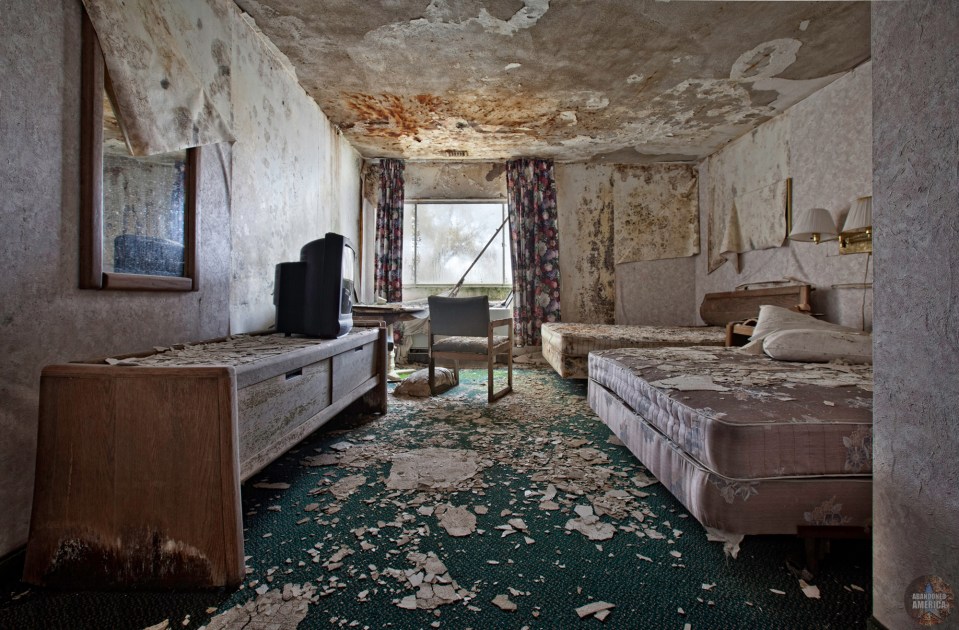 Interior of an abandoned hotel room with damaged walls, furniture, and carpet.