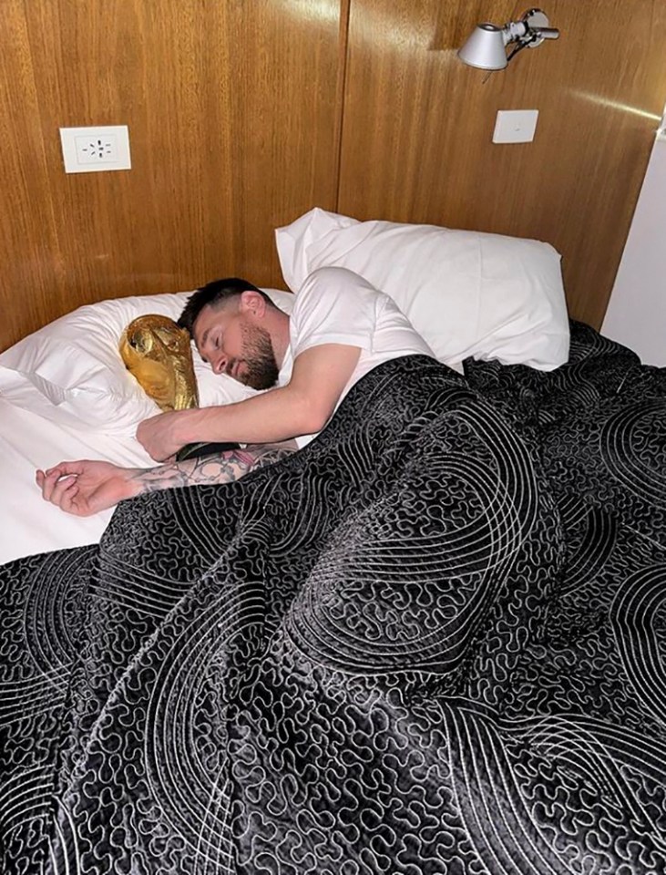 Lionel Messi asleep in bed with the FIFA World Cup trophy.