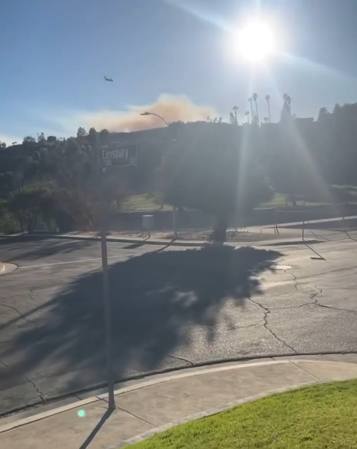 Smoke from a fire visible in the distance, with a plane flying overhead.