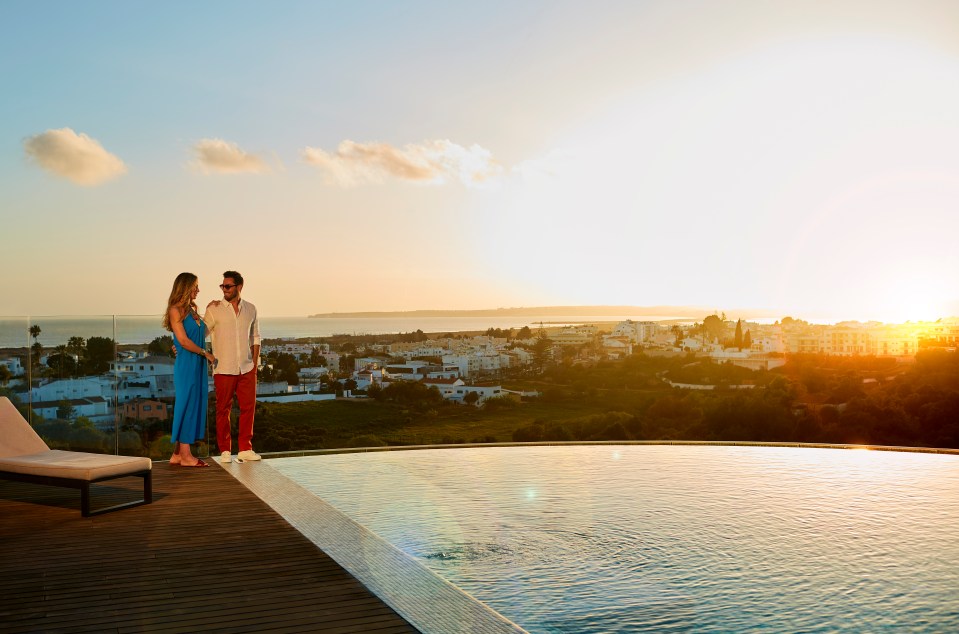 Couple by infinity pool overlooking town at sunset.