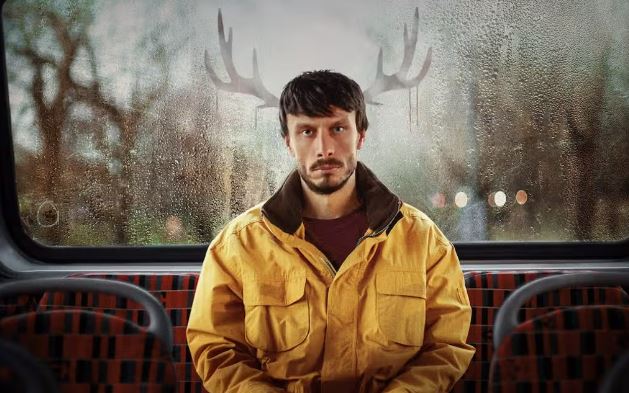 Man in yellow jacket on bus with reindeer antlers superimposed on window.