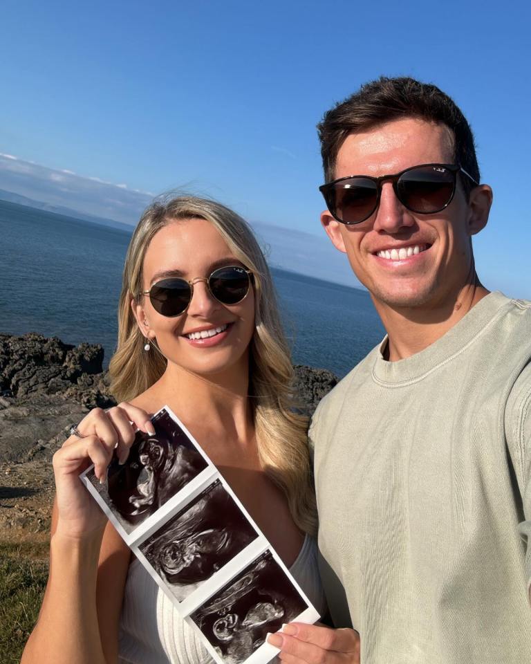 Couple holding ultrasound images by the ocean.