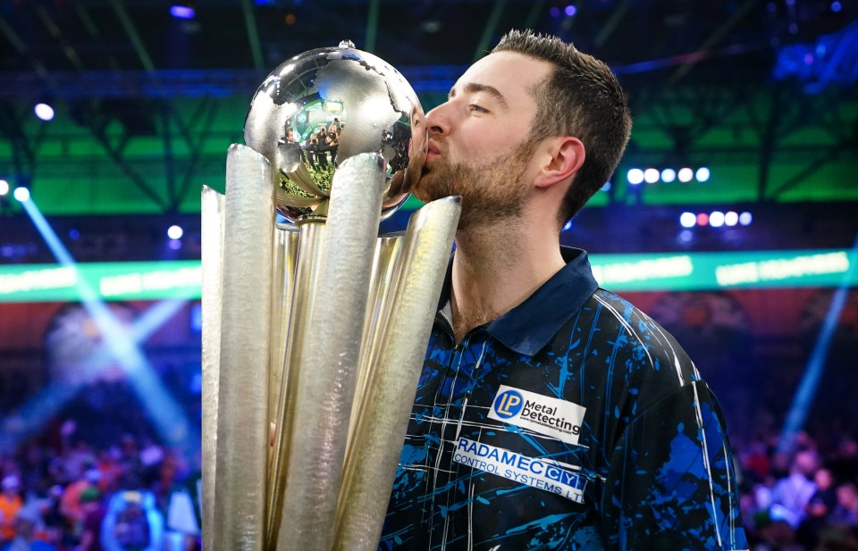 Luke Humphries kissing a trophy after winning a darts championship.