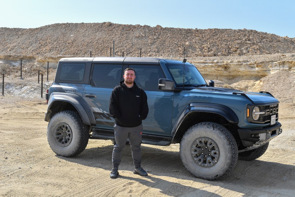 Man standing next to his Ford Bronco Raptor in a desert.