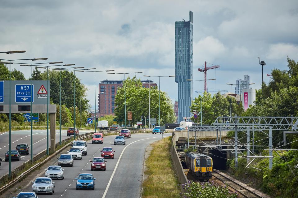 Motorway traffic with a train passing under an overpass, Beetham Tower in the background.