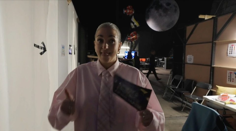 Macy Gray giving a thumbs-up while holding a card backstage.