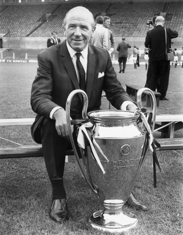 A man in a suit sits on a bench with the European Cup.