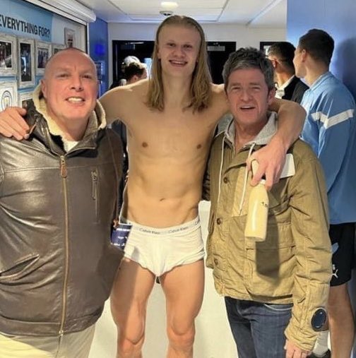 Erling Haaland shirtless with Noel Gallagher and another man in a dressing room.