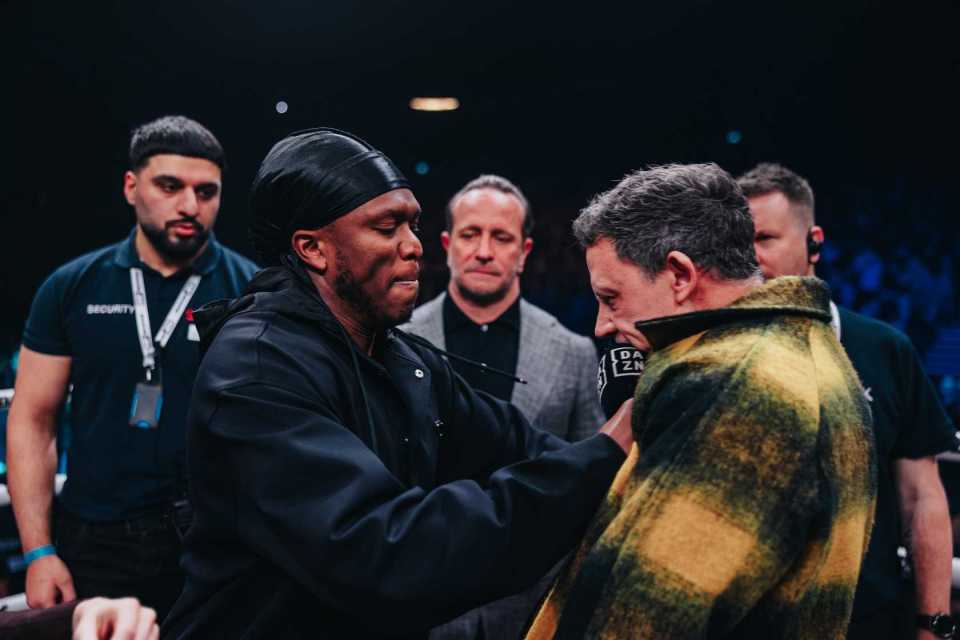 A man in a black jacket helping another man into a plaid jacket.