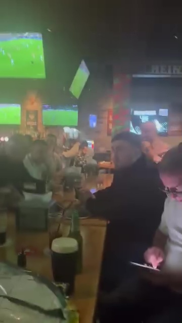 A man in a cow costume surprises Luke Littler with a birthday cake at a bar.