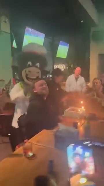 Luke Littler surprised with birthday cake by a person in a cow costume.