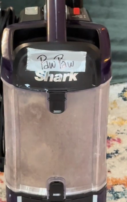 Shark vacuum cleaner with a label that says "Paw Paw" and a dust cup full of dirt.