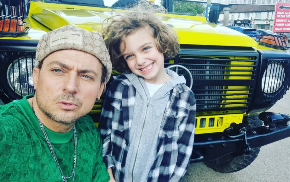 Paul Danan and his son DeNiro posing in front of a yellow car.