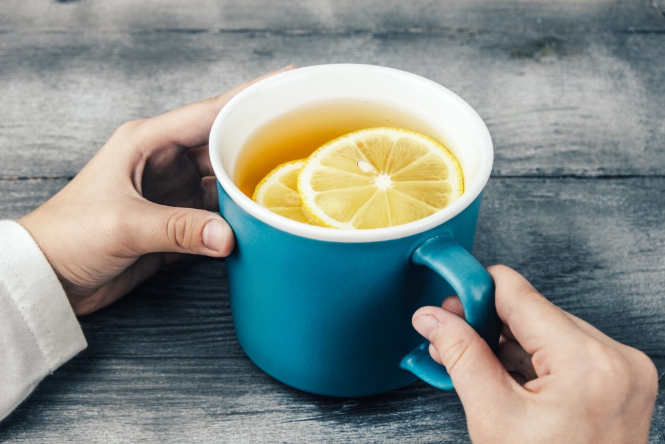 Woman's hands holding a blue mug of tea with lemon slices.