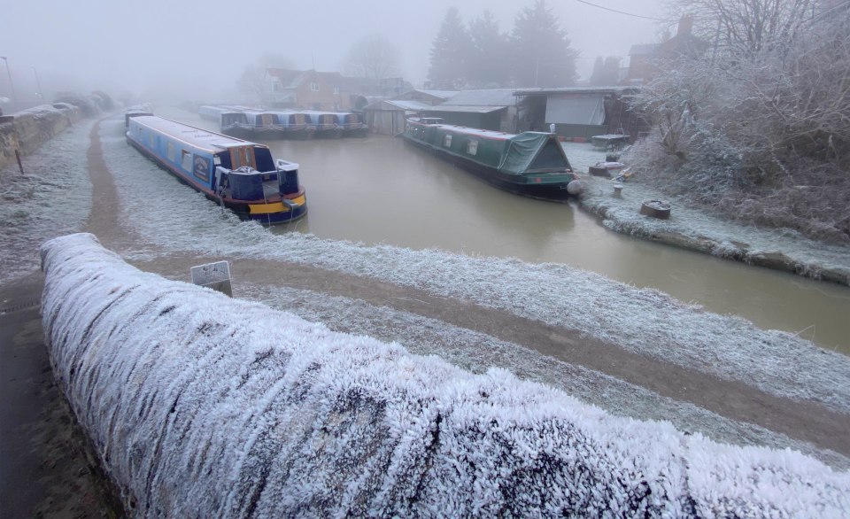 Frozen narrowboats on a foggy canal.