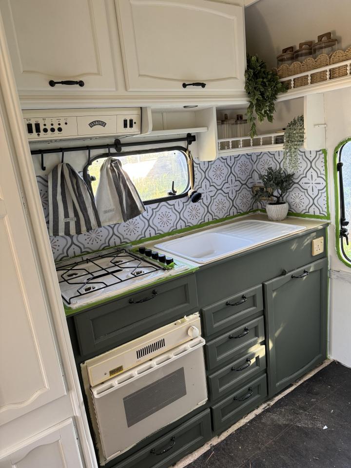 Renovated caravan kitchen with dark green cabinets and patterned backsplash.