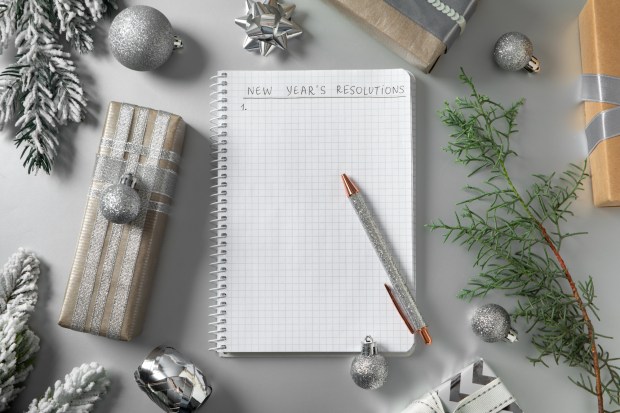 Notebook with New Year's resolutions list, pen, and holiday decorations.