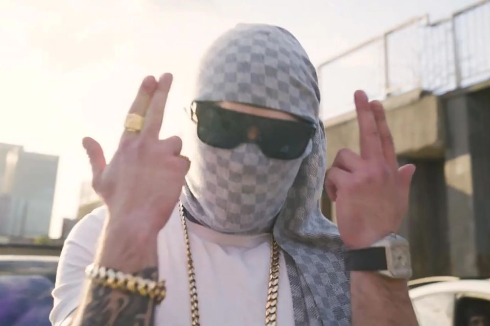 Person wearing sunglasses and a checkered scarf making a hand gesture.