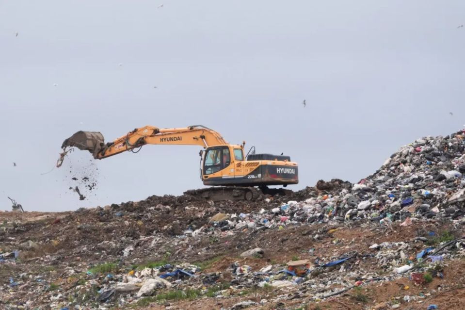 Excavator moving trash at a landfill.