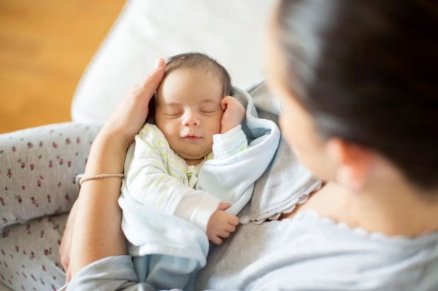 A mother cradles her sleeping newborn baby.