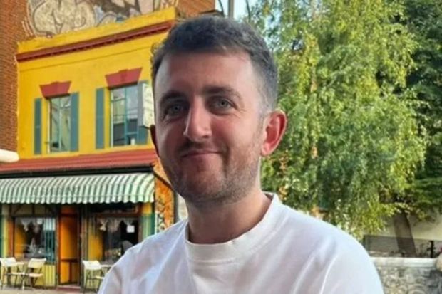 Man in white shirt in front of colorful building.